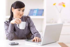 Девушка сидит за компьютером с чашкой чая